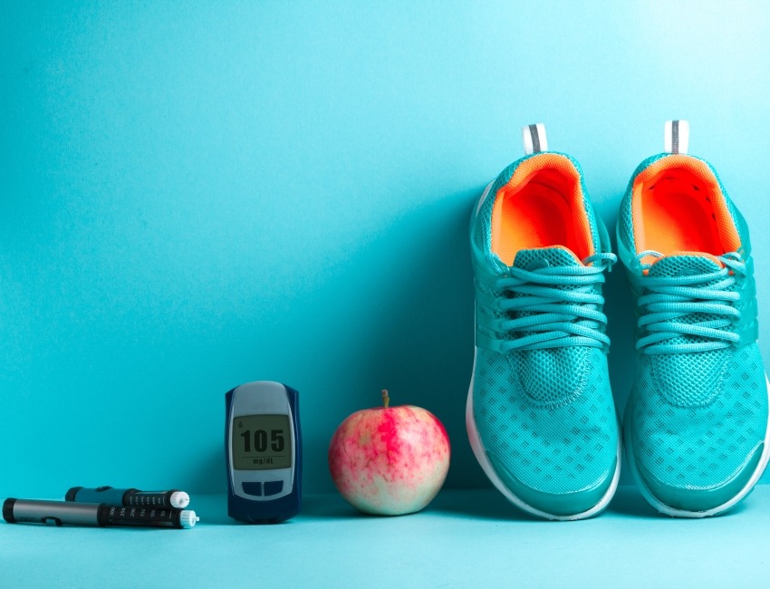 Plumas de insulina, un monitor de glucosa, una manzana y zapatos deportivos.