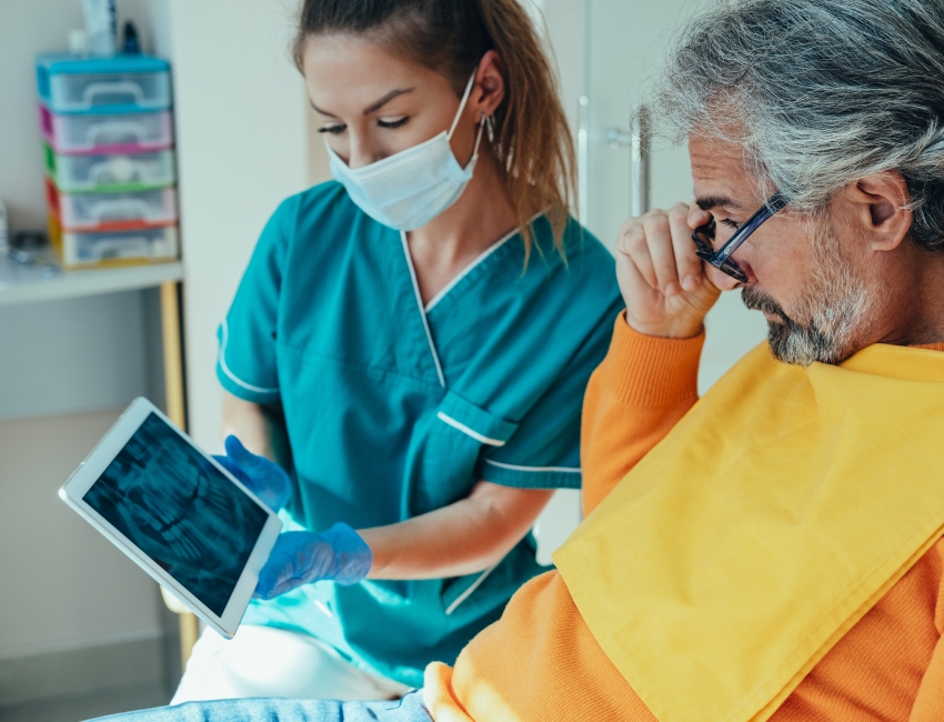 A man and health care nurse in a dentist office with a tablet.