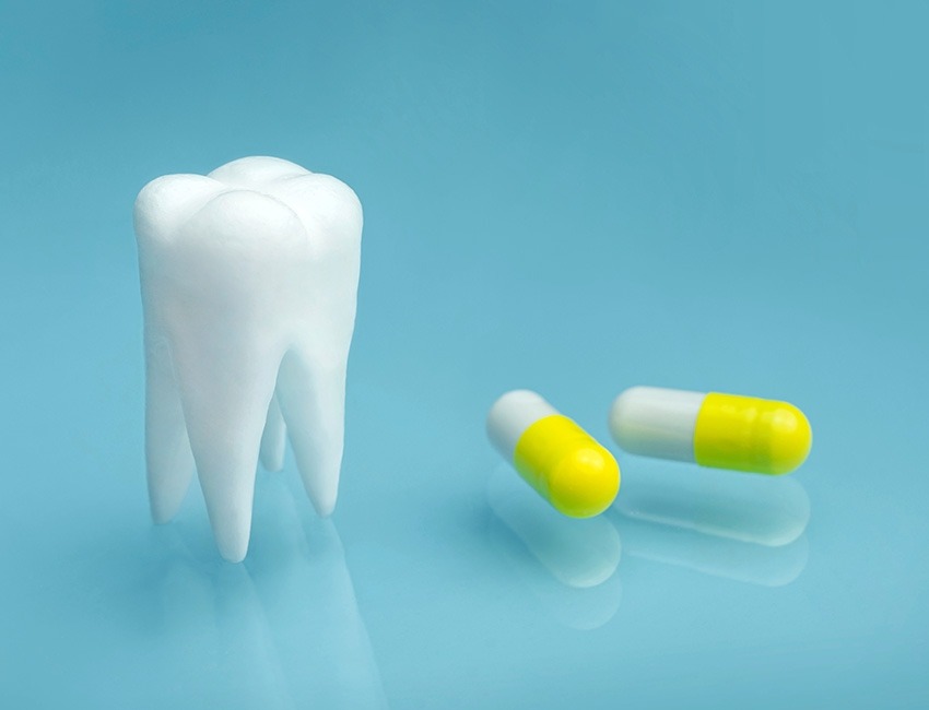 An tooth is sitting to the left of two pill capsules