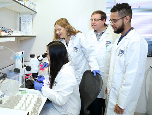 A group of scientists in lab coats analyzing an object under a microscope.