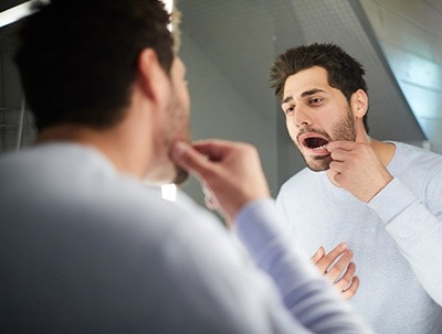 A man checking his teeth in front of a mirror.