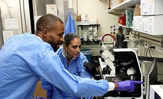 Two scientists in lab coats intently observing a microscope, engaged in research within a laboratory environment.