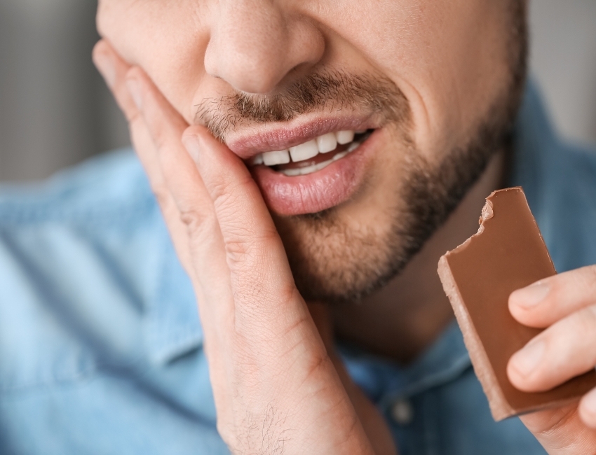  Man experiencing toothache while biting into chocolate.