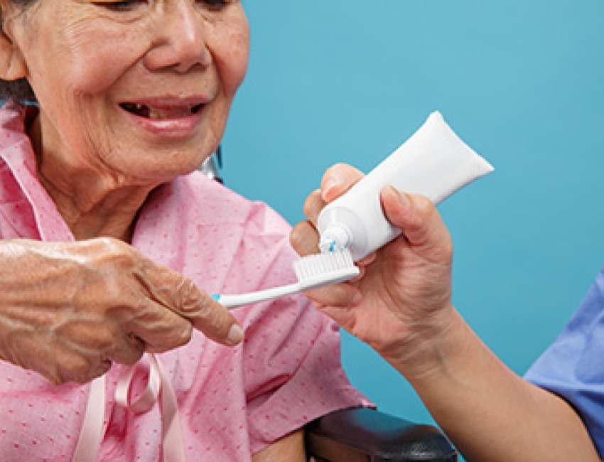 Caregiver helping older woman brush and floss teeth.