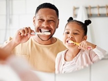 A father and daughter looking into the mirror brushing their teeth.