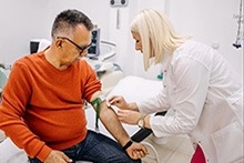 A medical professional using a blood pressure monitor on a male patient in a clinical setting.