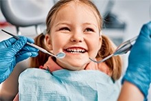 A young girl happily sits in a dentist chair, smiling as she receives dental care.
